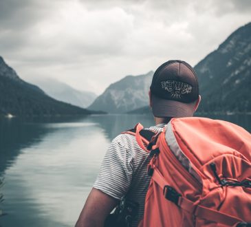 Man wearing backpack looking out at lake.