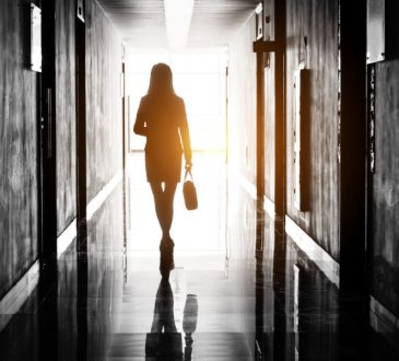 Silhouetted woman walking down hallway of office building