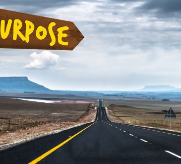 The Word Purpose written on a Sign Pointing Towards a Long Road