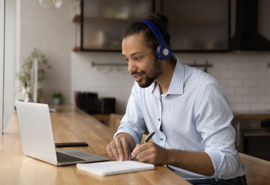 Man taking notes while watching video on laptop