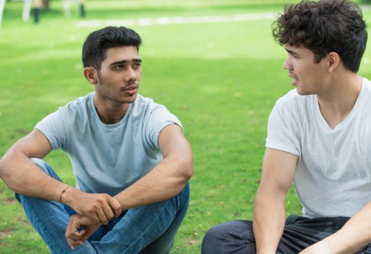 Two men sitting on grass talking
