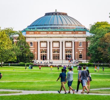Students walking outdoors on university campus with big green field
