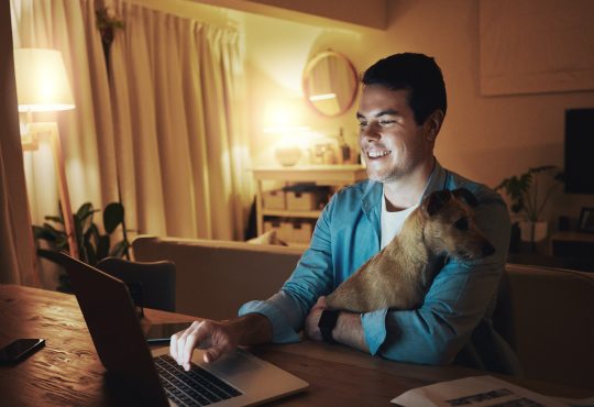 Man working on laptop at home with dog in lap