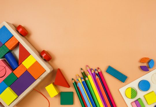 Colorful cubes, paints, pencils, blocks, modeling clay on orange background.