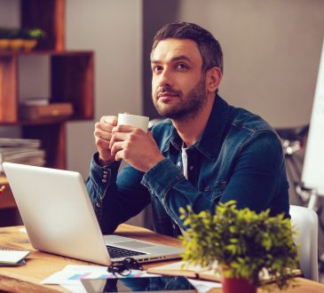 Man sitting at desk drinking coffee and daydreaming