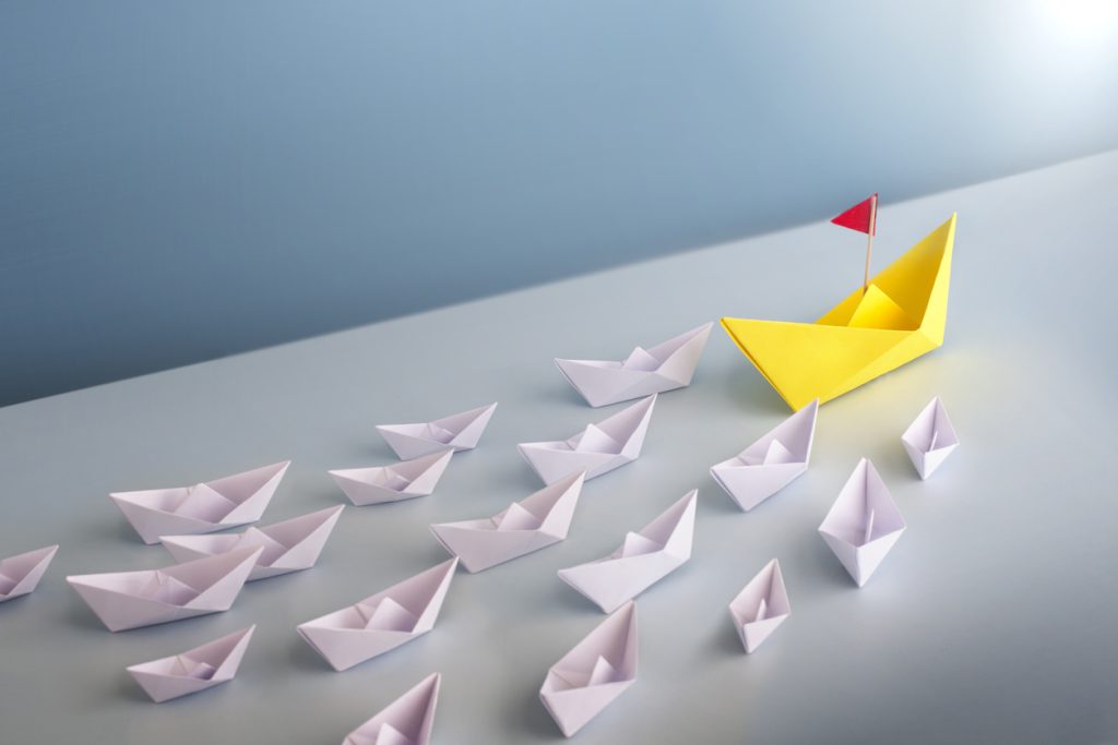 A group of white origami boats led by a bigger yellow boat