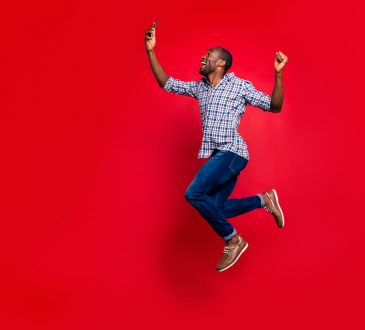 Side profile of man jumping in air holding cellphone on red background