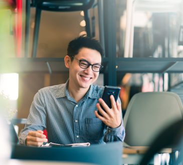 Businessman smiling and looking at cellphone while sitting at desk with laptop