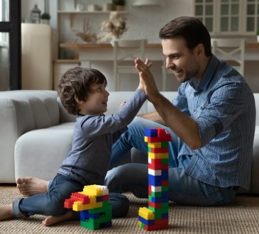 Dad high fiving young son while playing with blocks on carpet