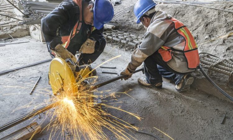 Two construction workers cutting pipe