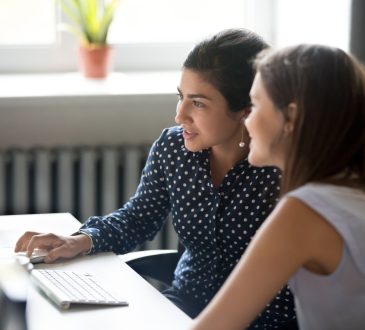 Smiling female colleagues work together at computer