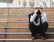 Businessman sitting on stairs outside with head in hands