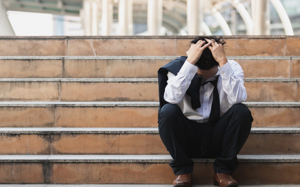 Businessman sitting on stairs outside with head in hands