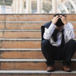 Businessman sitting on stairs outside with head in hands