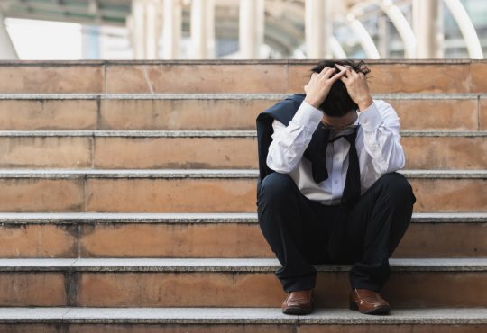 Businessman sitting on stairs outside with head in hands