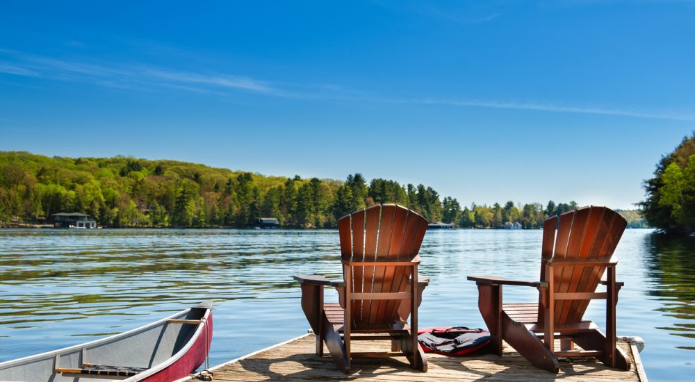 Two Muskoka chairs on a wooden dock overlooking the blue water of a lake in Muskoka, Ontario