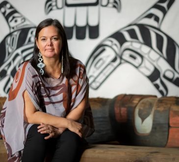 Christy Smith sits in front of Indigenous art on wall.