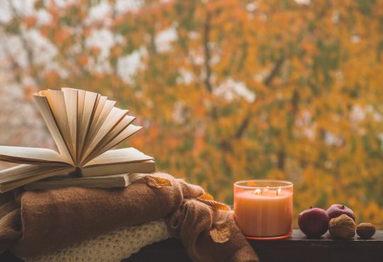 Autumn books scene - books in front of fall leaves, on top of blankets, beside candle