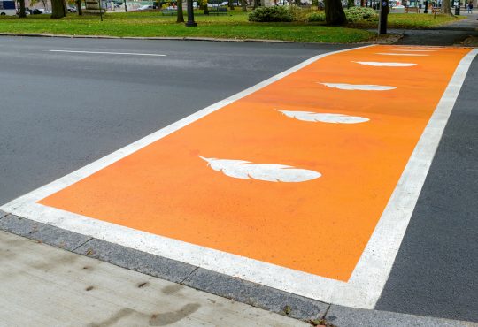 Crosswalk painted orange with white feathers for Truth and Reconciliation