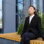 Businesswoman performing breathing exercises on bench outside