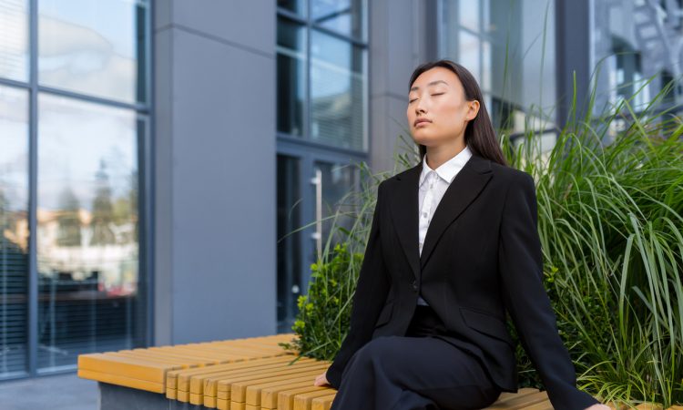 Businesswoman performing breathing exercises on bench outside