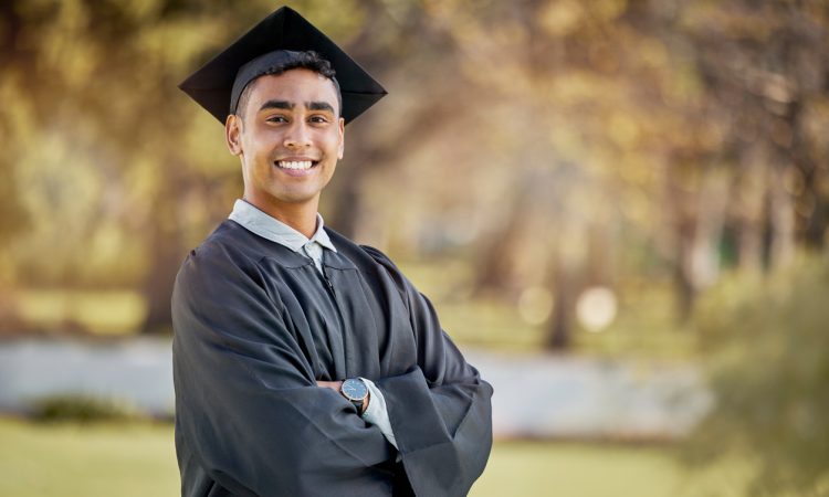 Young man posing for photo outdoors wearing graduation cap and gown