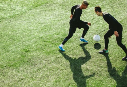 tWO MEN PLAYING SOCCER ON FIELD OUTDOORS