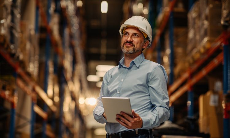 Manager with safety helmet holding digital tablet in warehouse