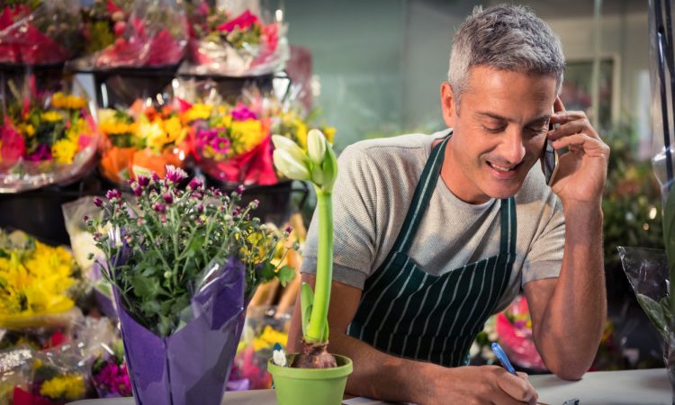 Male florist taking order on mobile phone at his flower shop