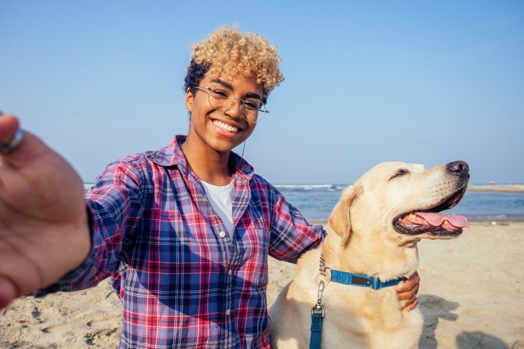 Woman taking selfie with golden lab dog at the beach.