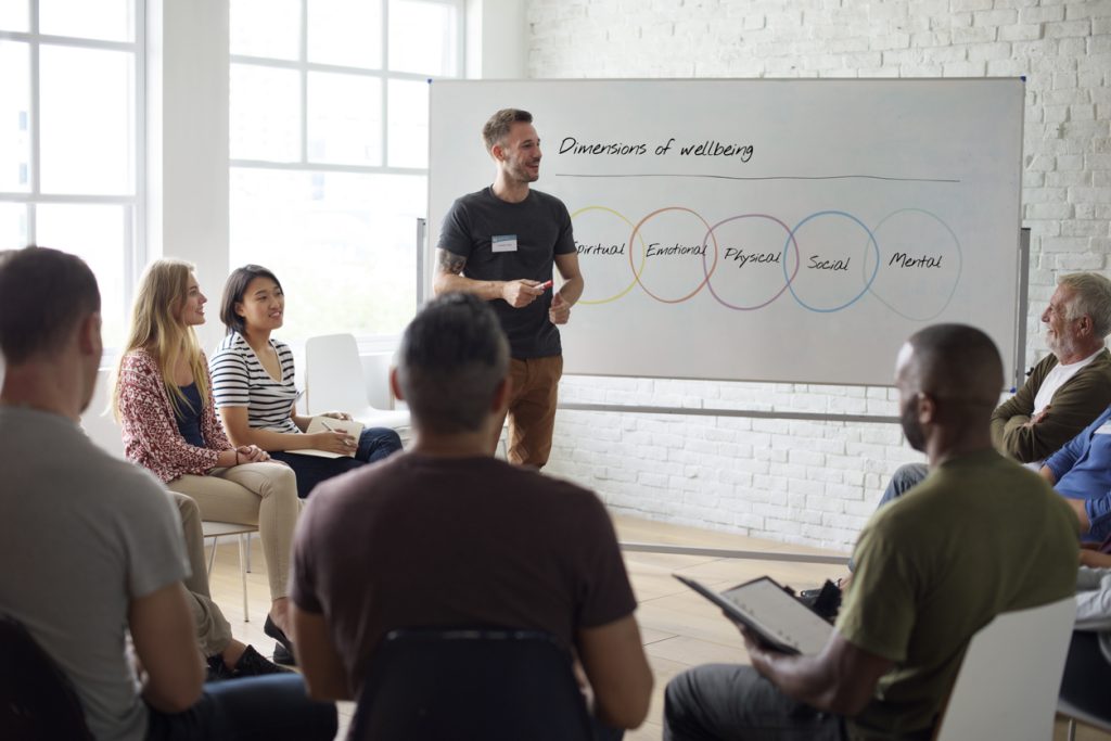 Man presenting office seminar on well-being using whiteboard