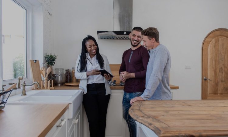 Black female real estate agent in kitchen showing gay couple around new house.
