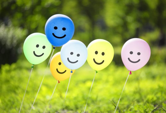 Smiley face balloons hovering over grass