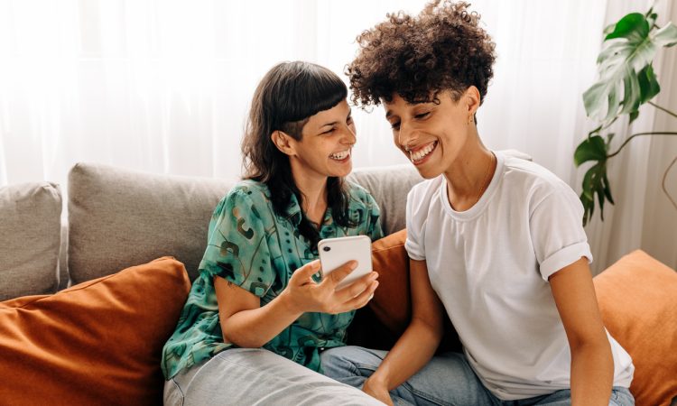 Lesbian couple laughing on couch together at home.
