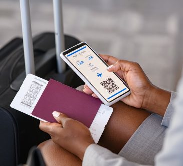 Close up hand of black businesswoman checking flight eticket on phone while holding passport and boarding pass.