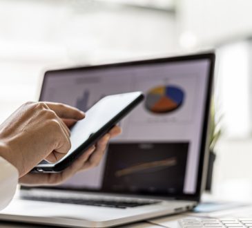 Woman texting on phone in front of open laptop