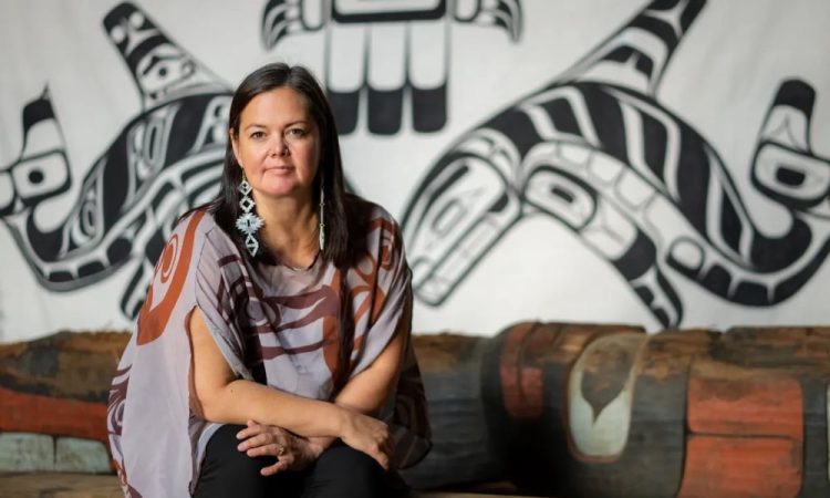 Woman sitting in front of Indigenous artwork on wall.