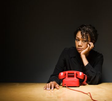 Woman sitting in front of phone on desk, looking discouraged