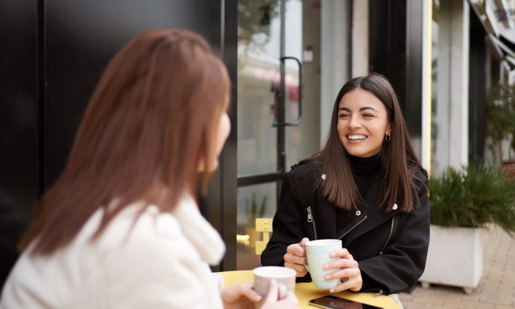 Two women having coffee on bistro table outside cafe
