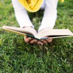 Person lying in grass reading book.