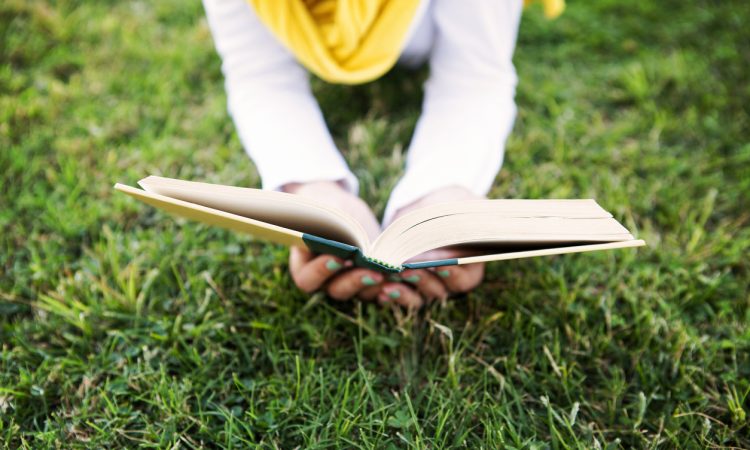 Person lying in grass reading book.