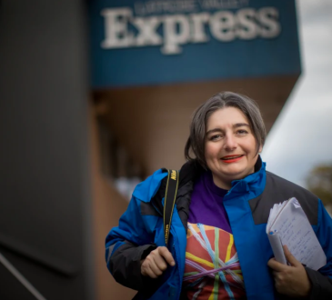 Woman standing outside newspaper office holding notebook