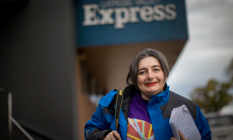 Woman standing outside newspaper office holding notebook