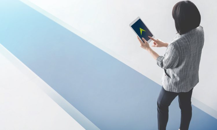 Woman walking on blue pathway looking at tablet with green arrow on screen pointing forward