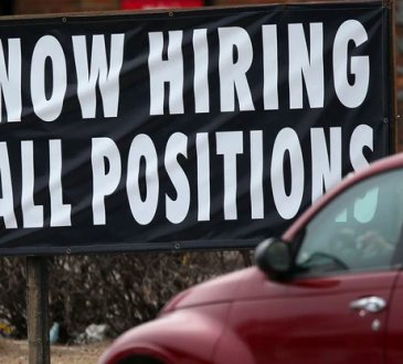 Car driving past large sign reading "NOW HIRING ALL POSITIONS"