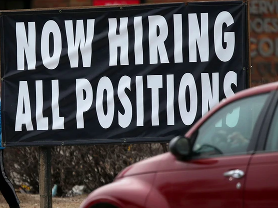 Car driving past large sign reading "NOW HIRING ALL POSITIONS"