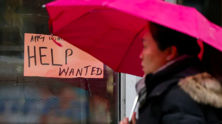 Woman with umbrella walking past store window with handwritten help wanted sign