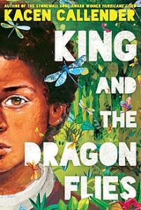 Book cover of King and the Dragonflies. This illustrated cover has the author's name Kacen Callender, at the top in yellow font. On the left half of the cover you can see part of a person's face. They have brown skin, brown eyes and dark brown hair. They are on a nature background, with green trees and grass and dragonflies flying around. The book title is in all caps and white down, and right-justified.