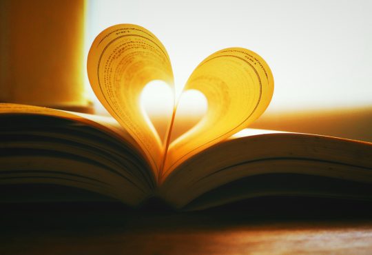 Book silhouetted by sun with middle pages folded into shape of a heart