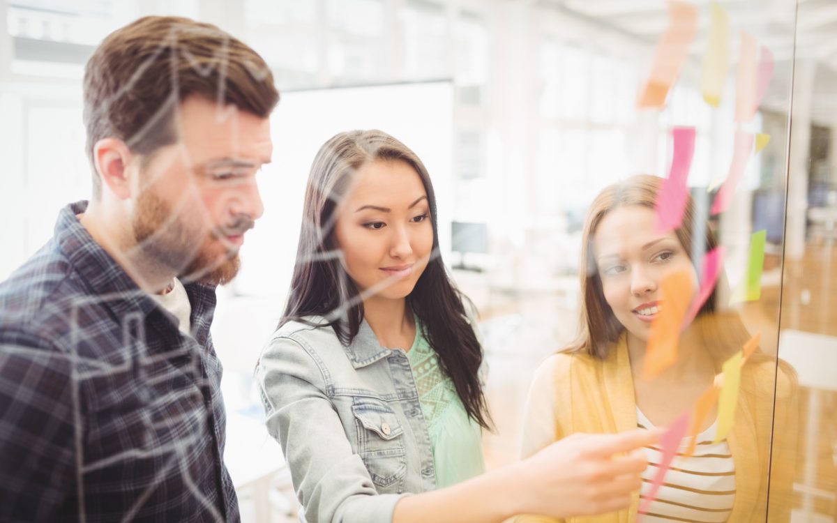 Three co-workers putting sticky notes on clear wall in office